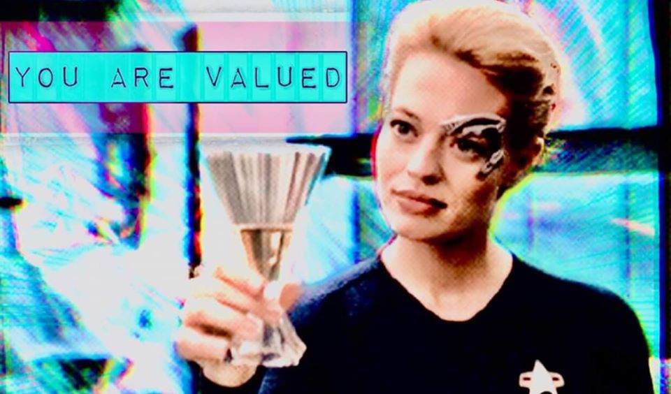 This meme is a screenshot from the TV show Star Trek: The Next Generation, featuring the character Deanna Troi, the ship's counselor, holding up a glass of wine. The text "You are loved" is written in a playful, cursive font above her head, while the text "You are valued" is written in a similar font below her head. The image is meant to be humorous and ironic, as Deanna Troi is known for her empathic and intuitive nature, but the phrase "You are valued" is often used in a more formal or professional context, making it a humorous contrast to the character's typically empathetic nature.